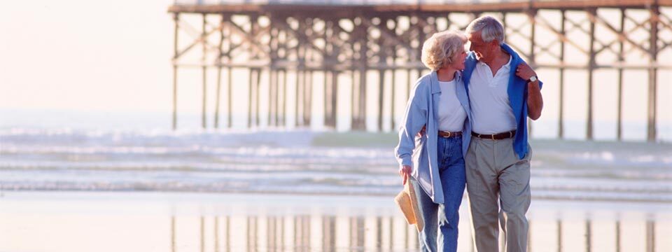 Older couple walking arm-in-arm by the seashore