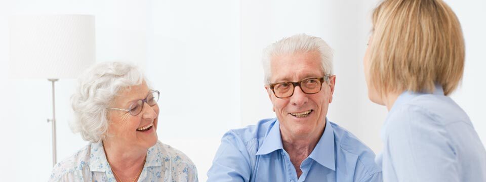 Two smiling senior citizens speaking with a younger woman