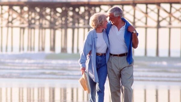 Older couple walking arm-in-arm by the seashore
